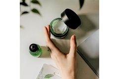 Image A hand reaching for a pot of face cream.